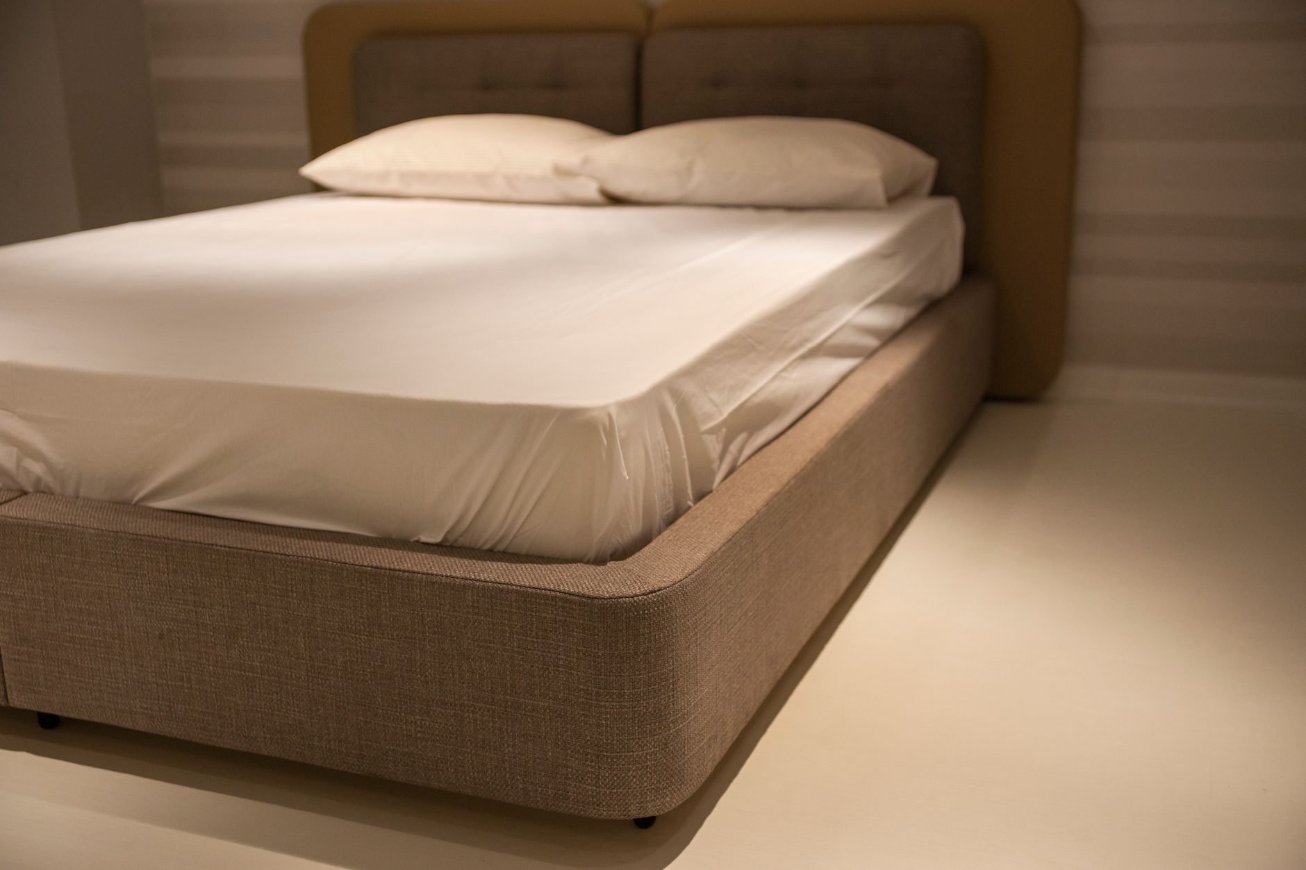 Cách dùng topper nệm để tăng độ êm. - A close-up view of a minimalist bedroom featuring a bed with white linen sheets and plush pillows.
