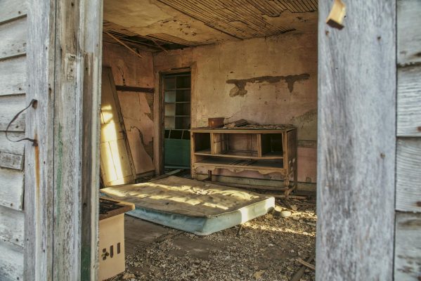 Các dấu hiệu nệm đã hư và cần thay mới - A rustic, abandoned room with a mattress and wooden dresser.