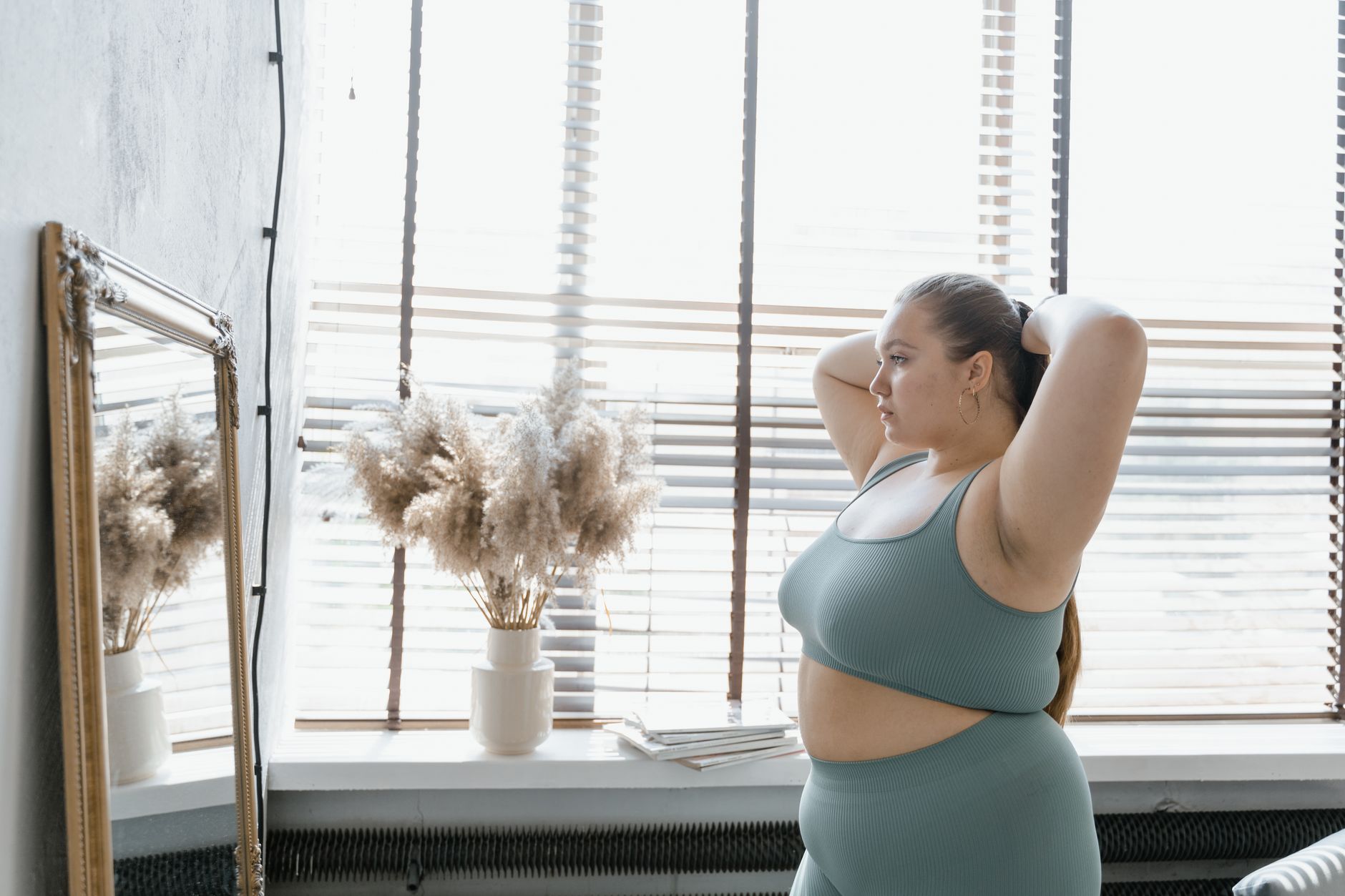 Nệm cho người béo phì trên 100kg - A plus-size woman in activewear admires her reflection indoors, promoting body positivity and self-esteem.