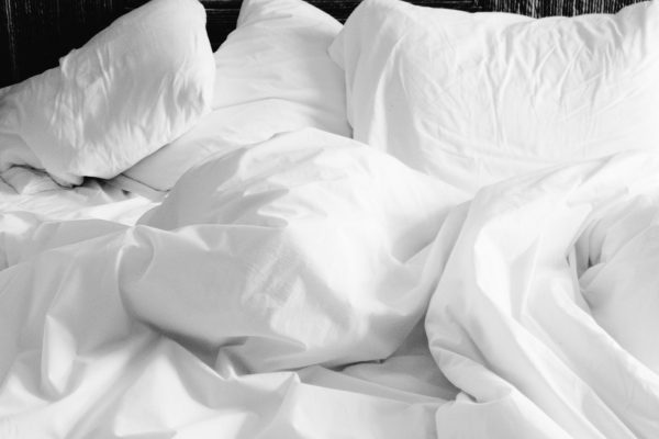 Cách diệt rệp giường trên nệm - A cozy, rumpled white bed with soft sheets and pillows in a modern bedroom setting.