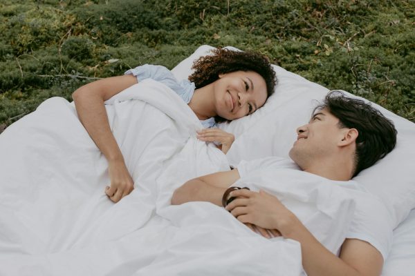 Cách dùng topper nệm để tăng độ êm. - Happy interracial couple lying on a white blanket outdoors, enjoying each other's company and nature.
