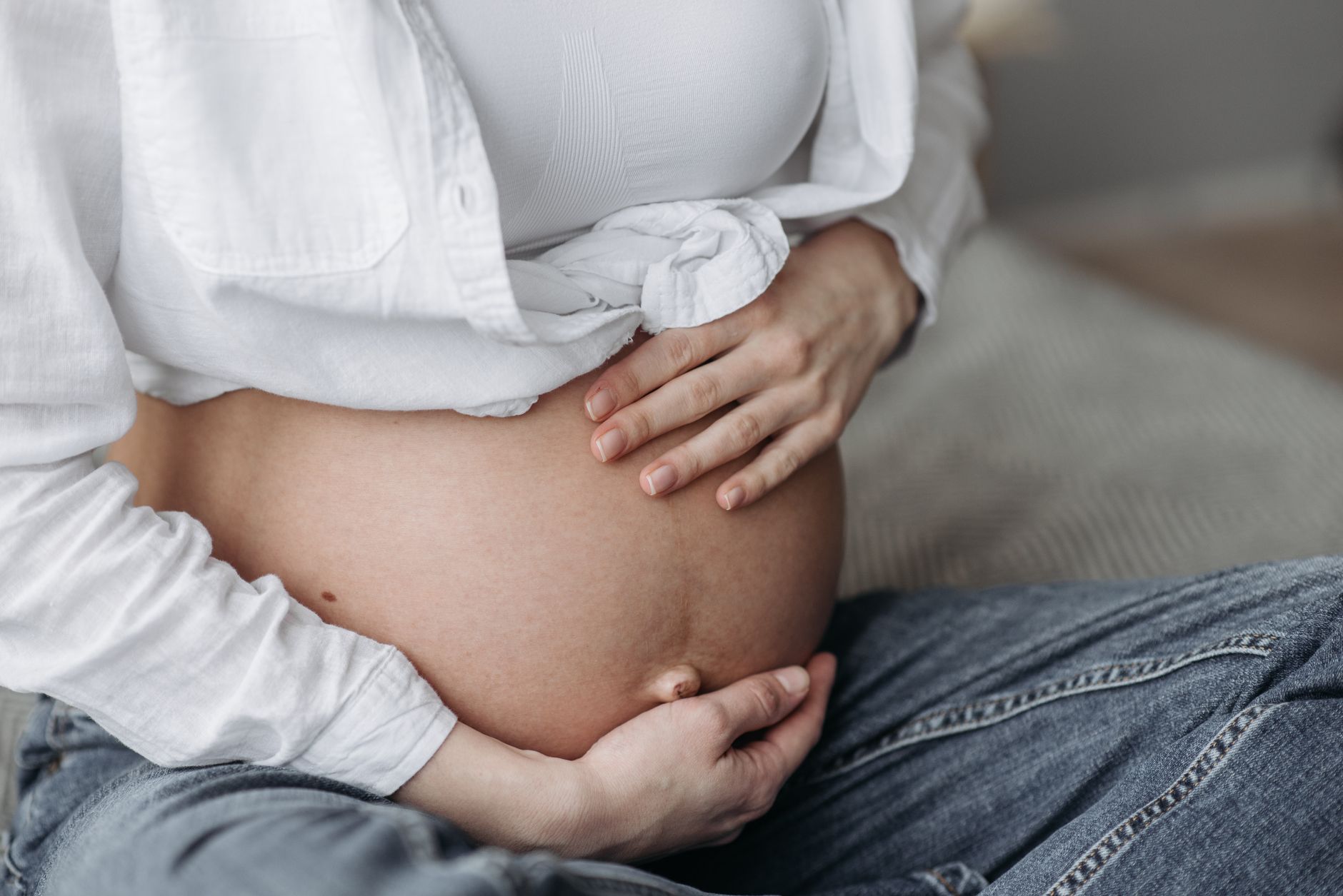 Nệm phù hợp cho bà bầu 3 tháng cuối - Close-up of a pregnant woman sitting, cradling her bare belly with both hands.