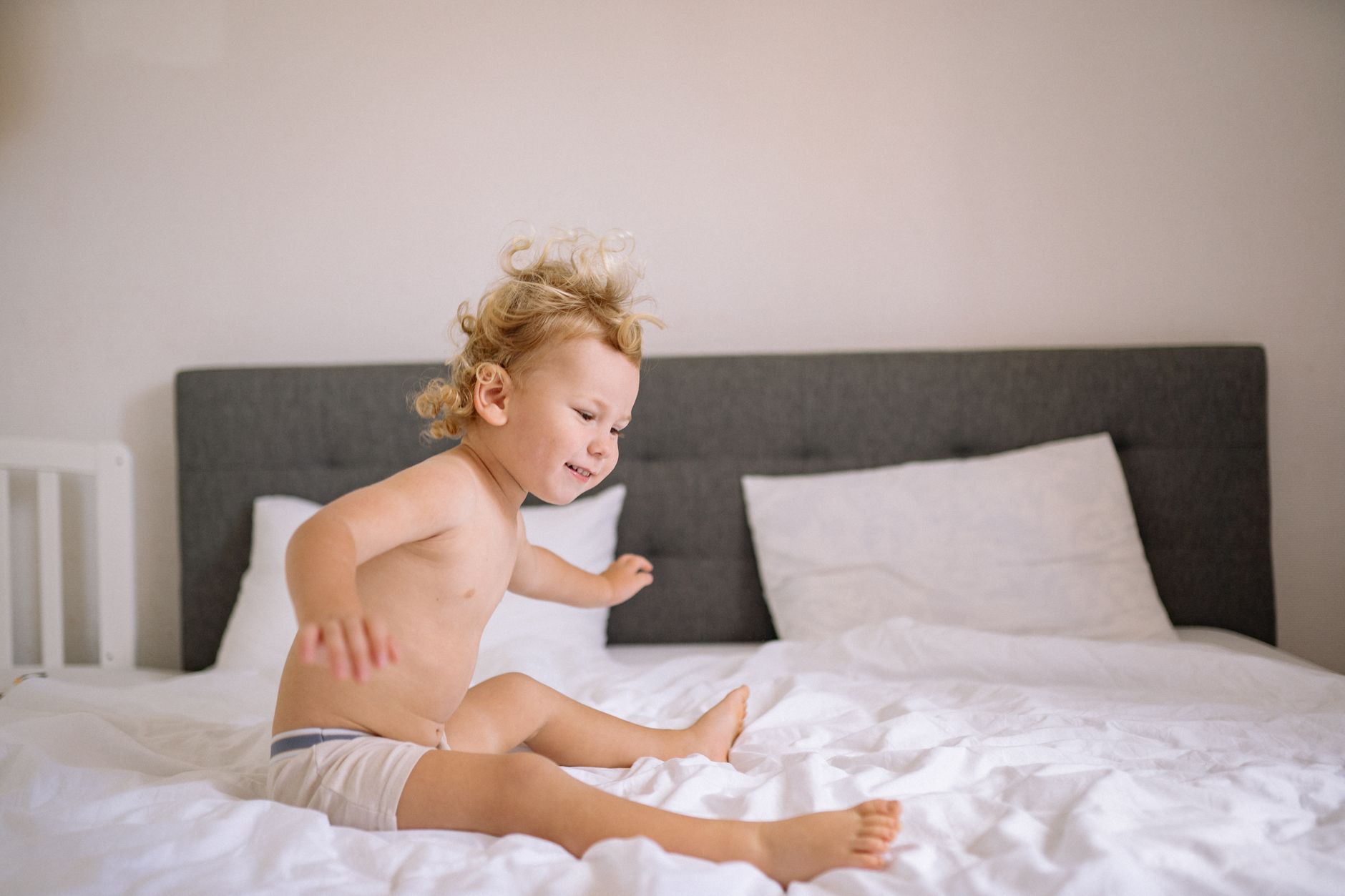 Nên chọn nệm gì cho trẻ sơ sinh - Smiling child energetically jumping on a bed in a cozy, well-lit bedroom, exuding joy.