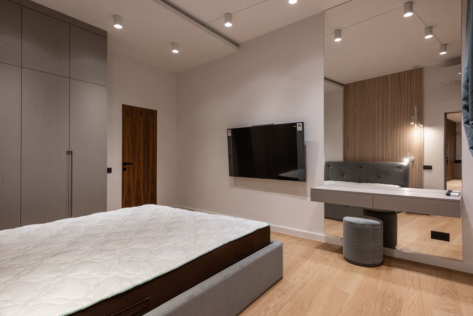 Nệm dày bao nhiêu cm là tốt nhất - Comfortable bed and wardrobe in modern bedroom placed in front of TV hanging on wall near dressing table with big mirror