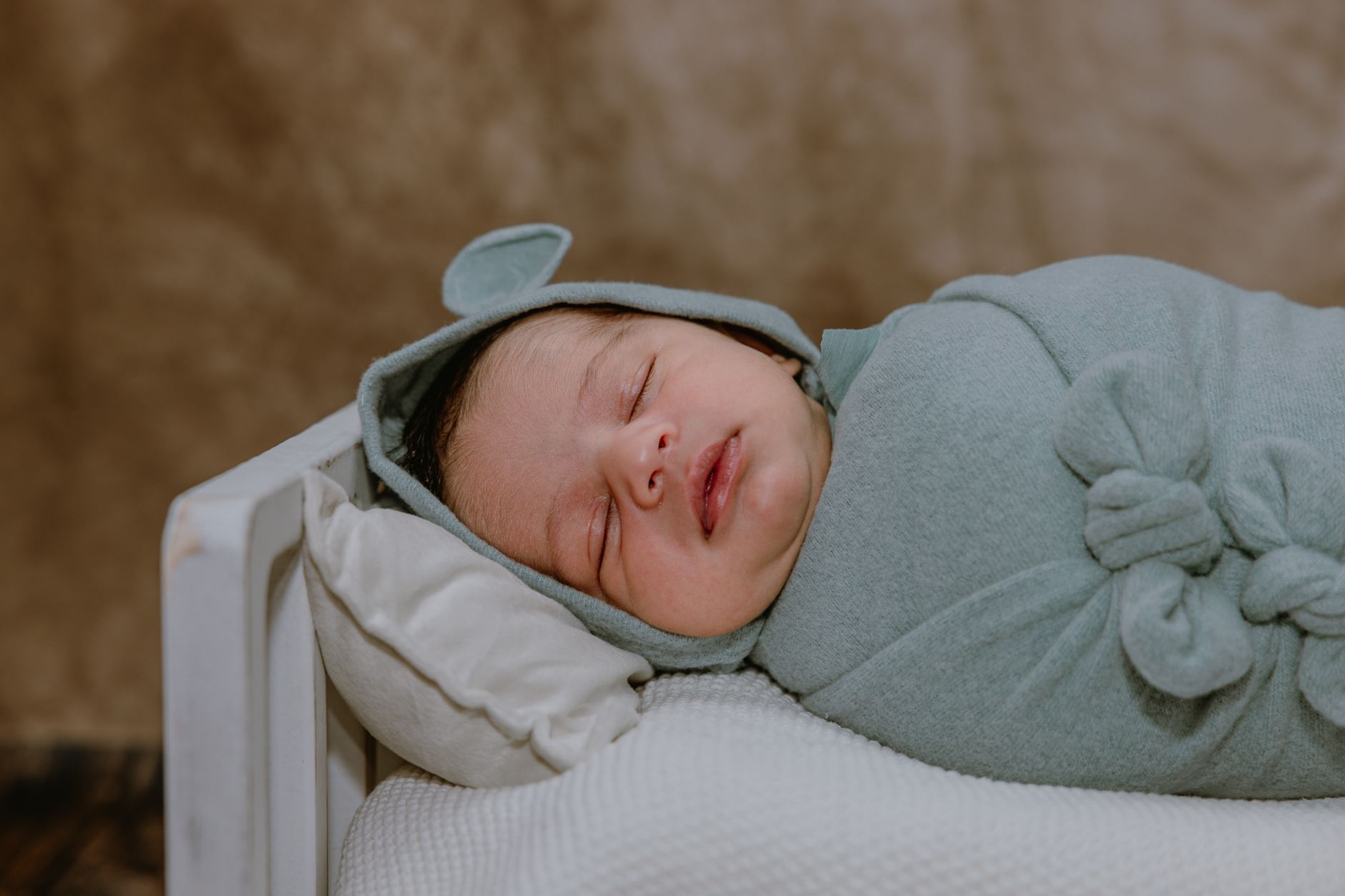 Nên chọn nệm gì cho trẻ sơ sinh - Adorable newborn baby peacefully sleeping in a soft green wrap on a small bed.