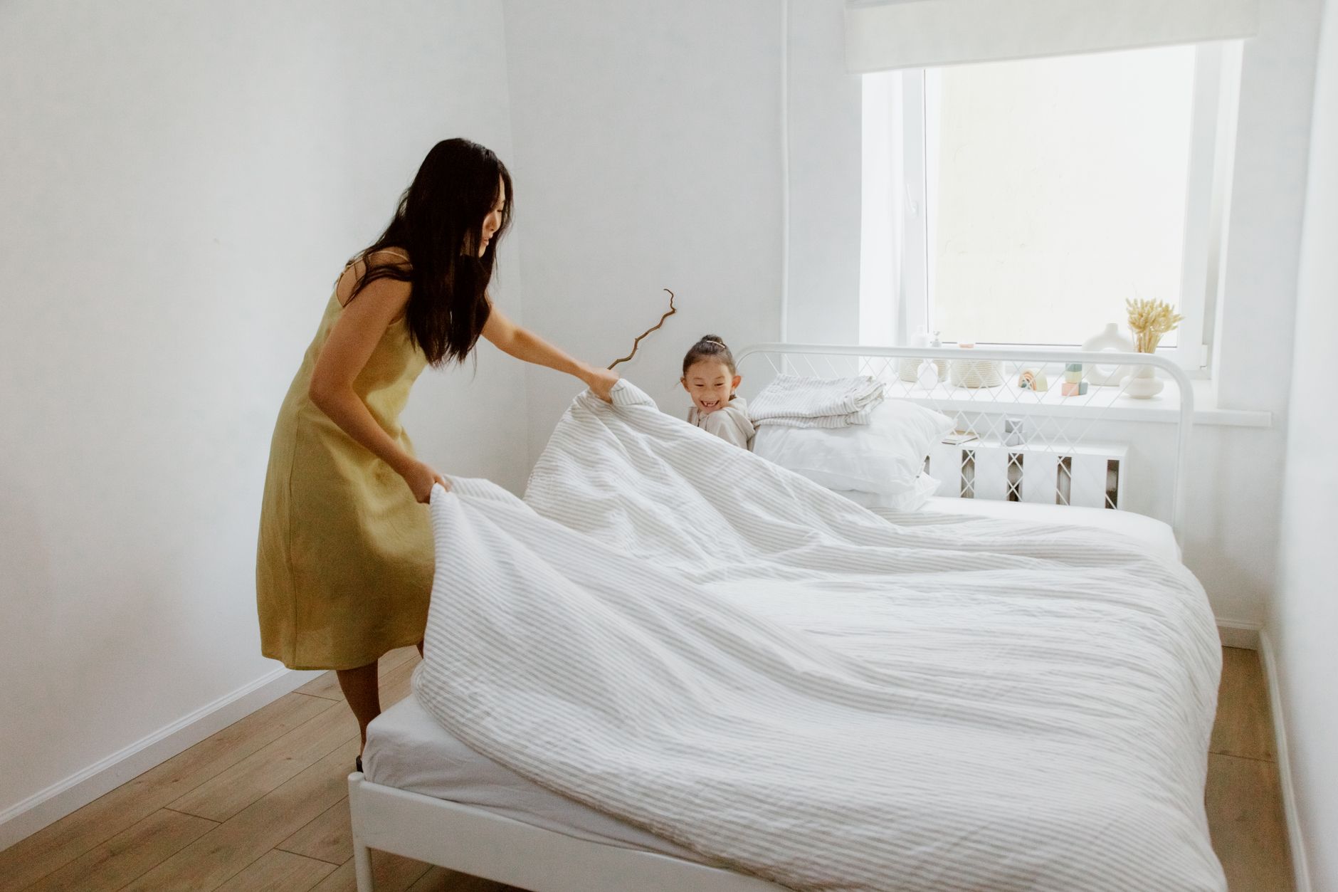 Cách diệt rệp giường trên nệm - A mother and daughter making the bed in a bright, airy bedroom with white walls.