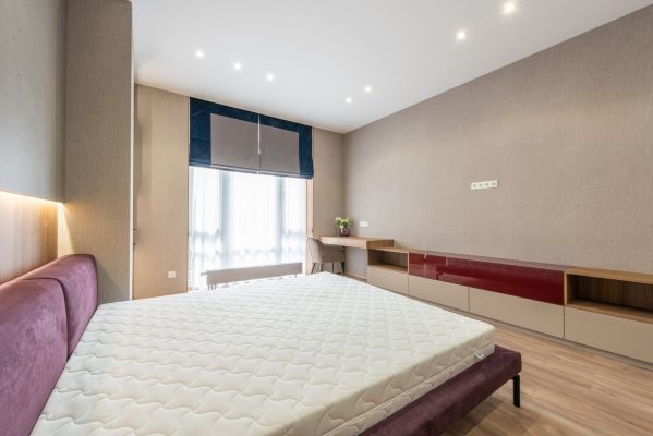 Mua nệm vào tháng nào rẻ nhất - Modern bedroom with white mattress on bed placed against wooden cabinet and table with flowerpot at wall with roller blind on window