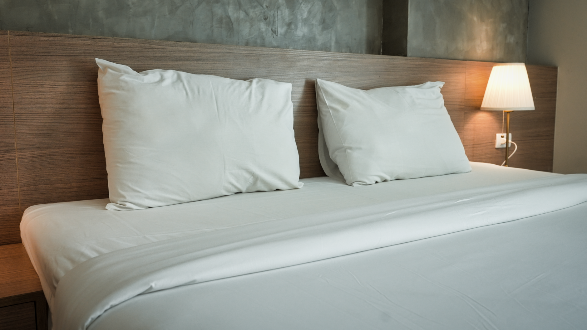 Nệm dày bao nhiêu cm là tốt nhất - A clean and contemporary hotel room featuring minimalist bedding and a warm bedside lamp.