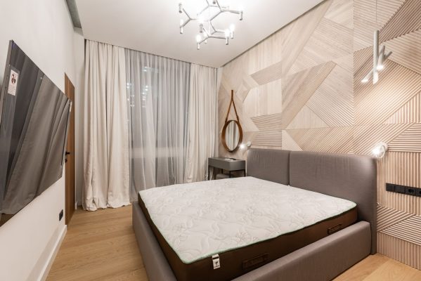 Nệm bị xẹp lún phải làm sao - Comfortable bed with mattress placed in front of modern TV in cozy bedroom with creative lamps and wooden floor