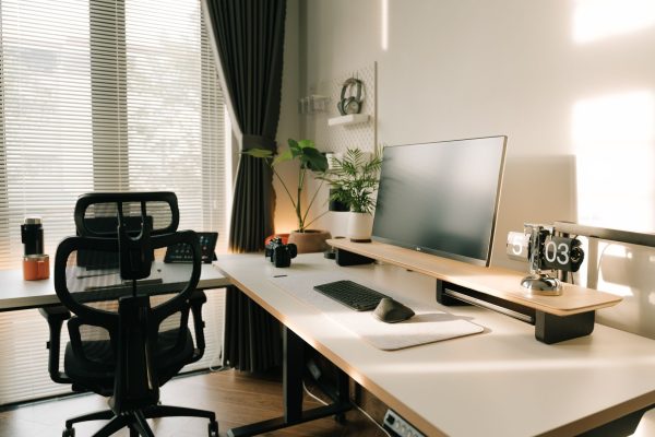 Nệm hỗ trợ cột sống cho dân văn phòng - Minimalist home office with ergonomic chair, desktop monitor, and plants in natural sunlight.