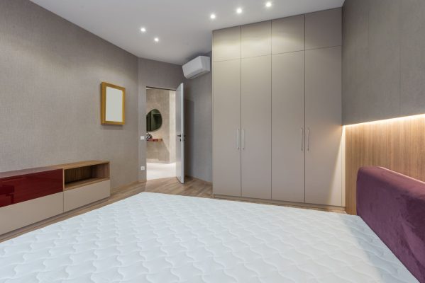 Nệm kháng khuẩn, nệm làm mát: công nghệ mới. - Interior of modern bedroom with white mattress on bed placed against cabinet near big closet and opened door in spacious apartment