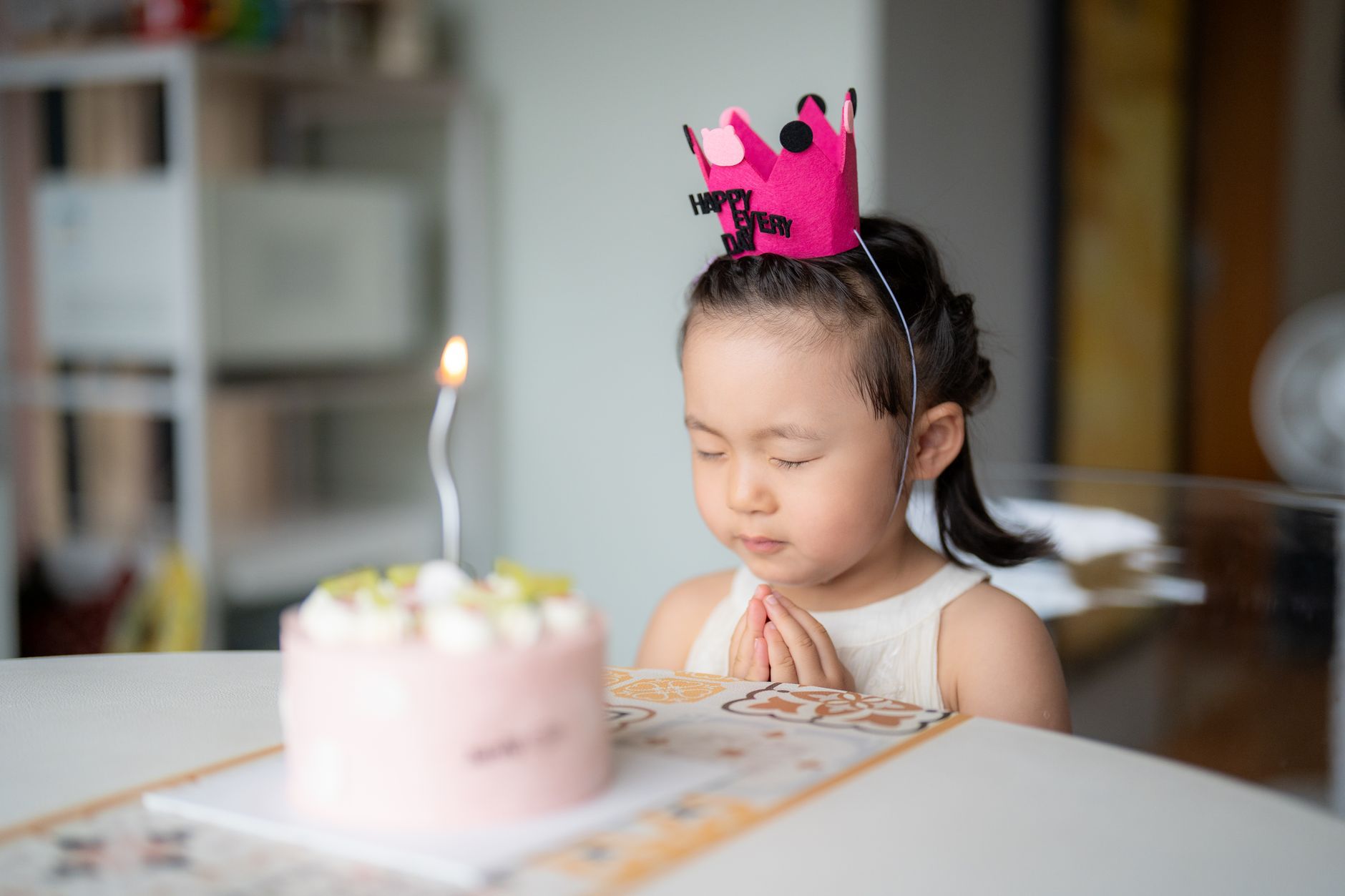 Trẻ em có nên nằm nệm memory foam - A young girl celebrates her birthday with a delightful pink cake and lit candle, wearing a festive crown.