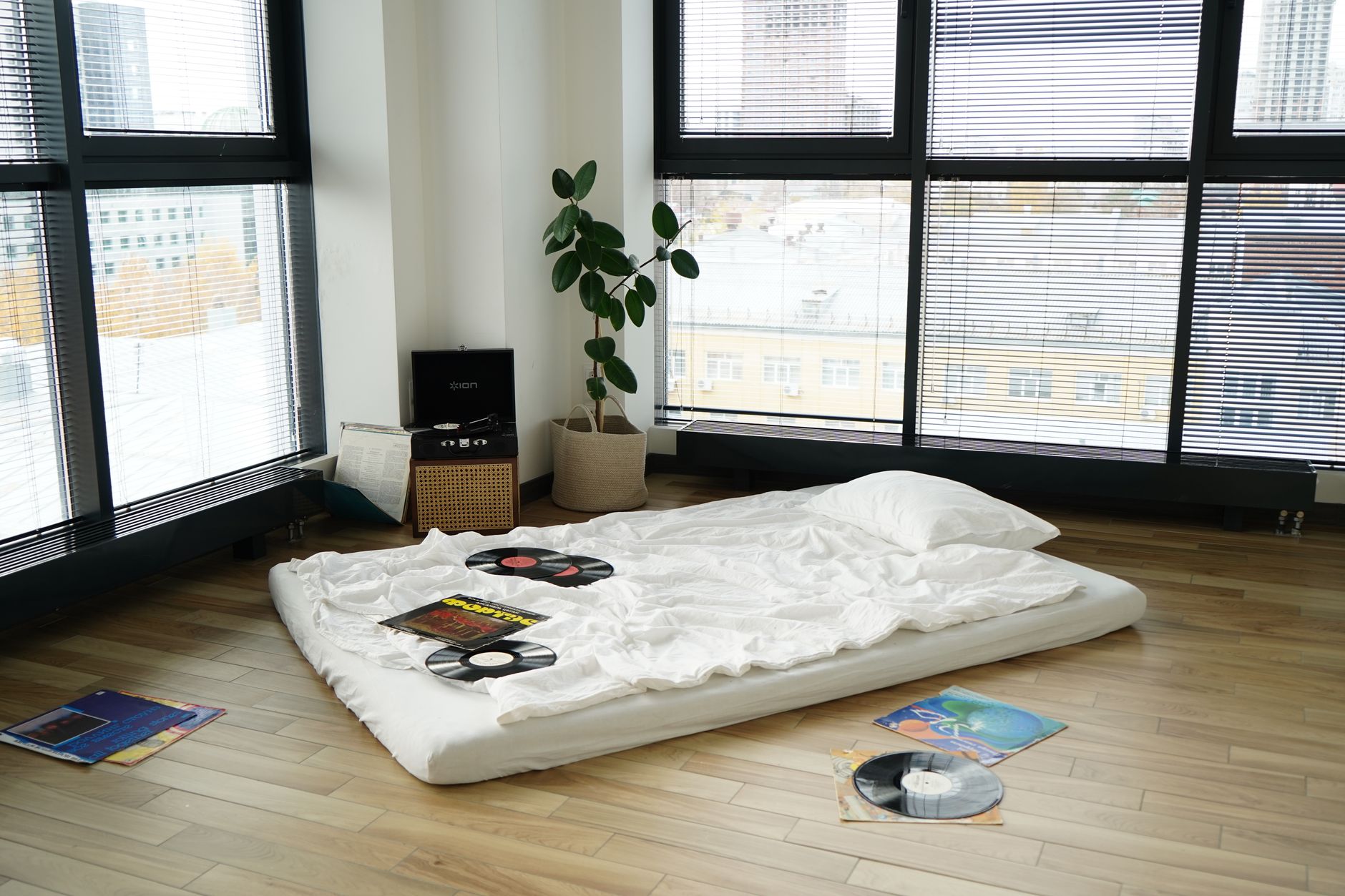 Nệm tốt cho học sinh sinh viên - A minimalist apartment interior with a mattress on the floor surrounded by vinyl records and a record player.