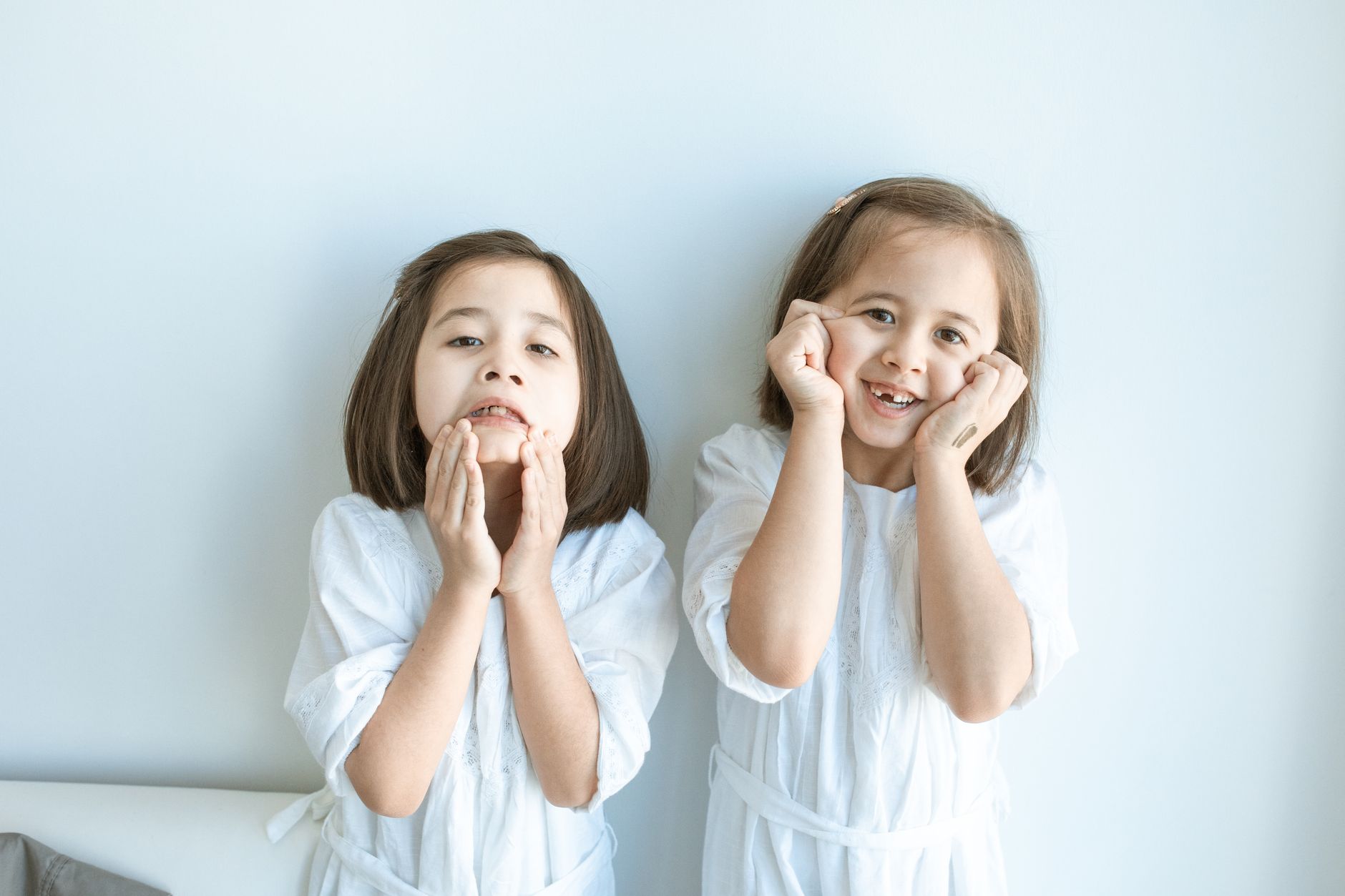 Trẻ em có nên nằm nệm memory foam - Two young sisters making playful faces indoors, exuding joy and innocence.