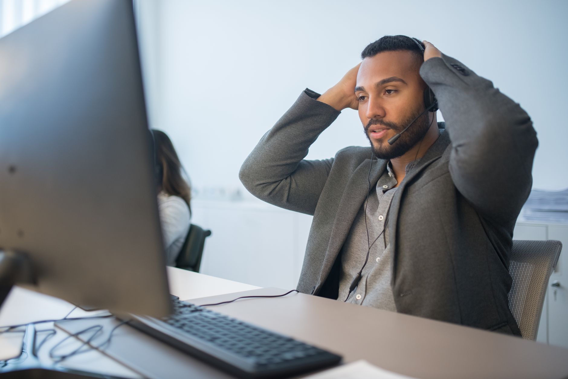 Nệm hỗ trợ cột sống cho dân văn phòng - Man in a headset working at a desk, hands on head, conveys work stress.