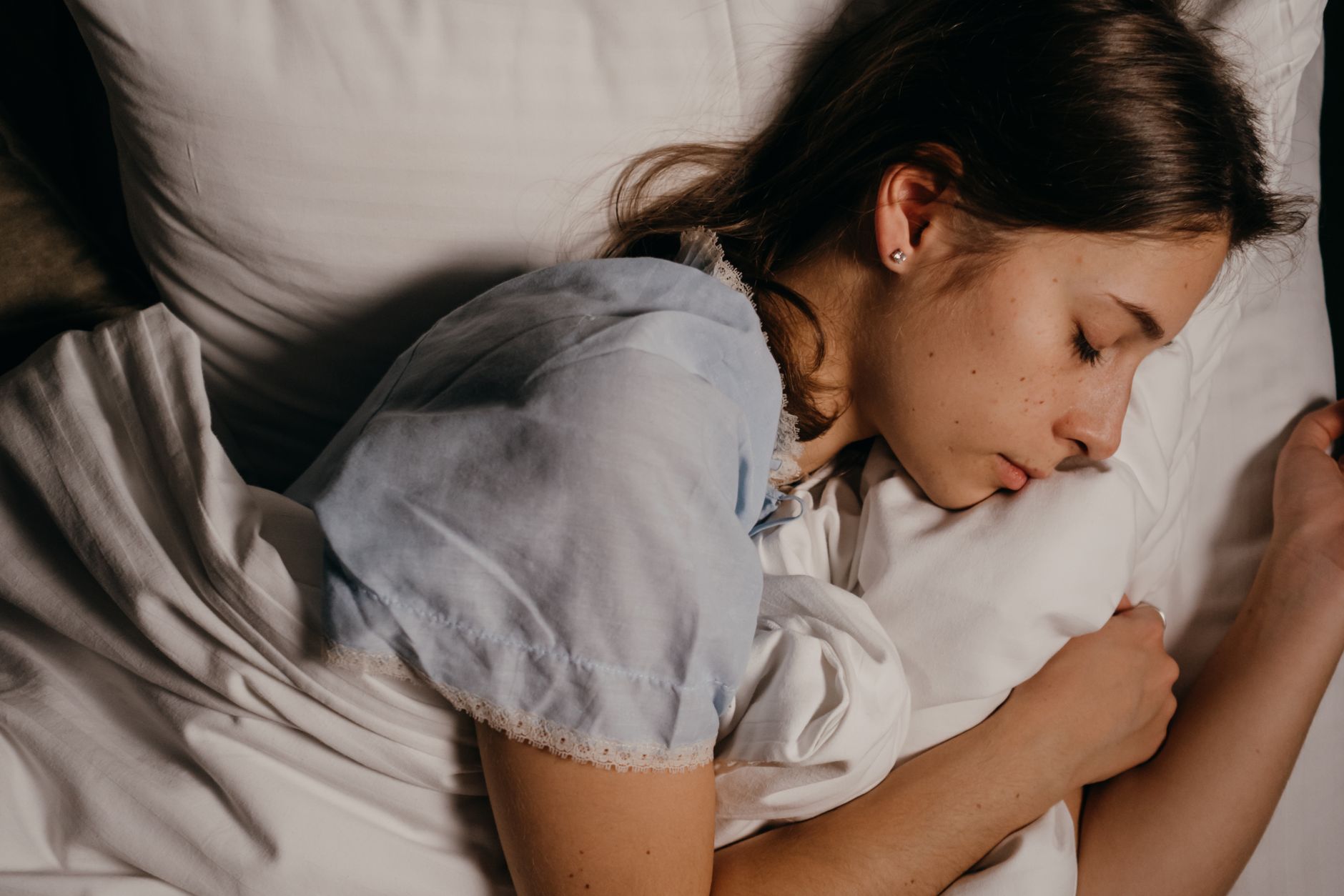 Cách dùng topper nệm để tăng độ êm. - A serene young woman peacefully sleeping on a white pillow indoors at night.