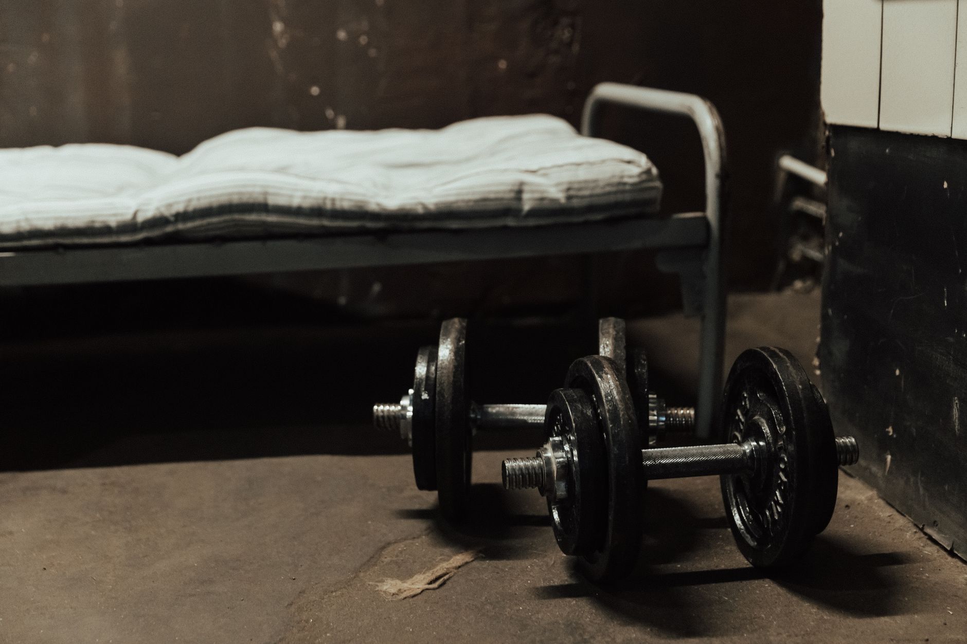 Nệm dày bao nhiêu cm là tốt nhất - A rustic gym scene featuring dumbbells next to a bed, highlighting home workout possibilities.