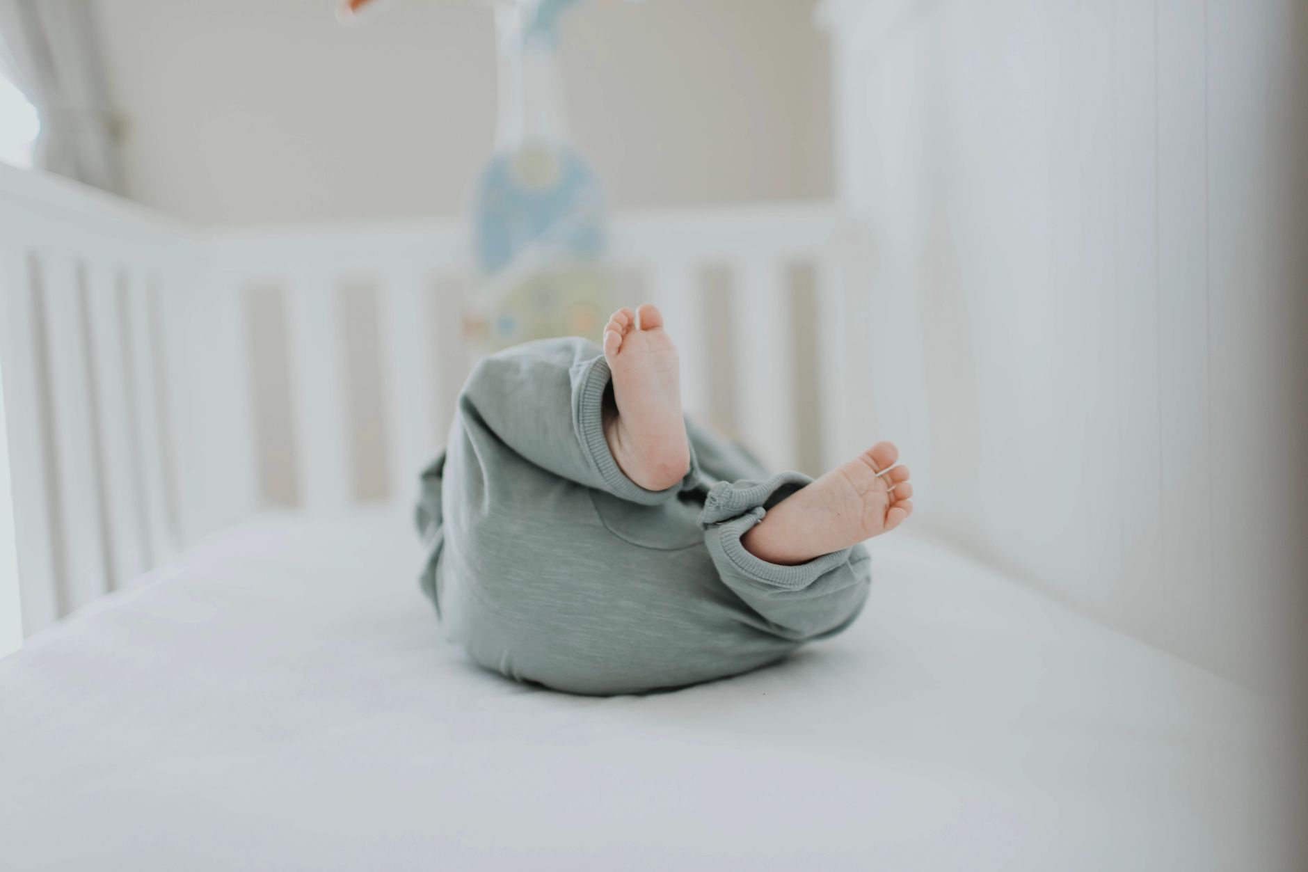 Nên chọn nệm gì cho trẻ sơ sinh - Cute baby feet in pajamas on a soft white crib. Perfect for children's room decor.